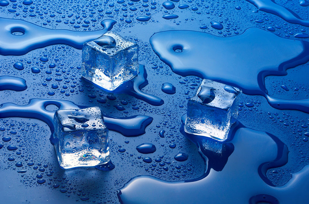 Three ice cubes sitting on top of a blue surface.